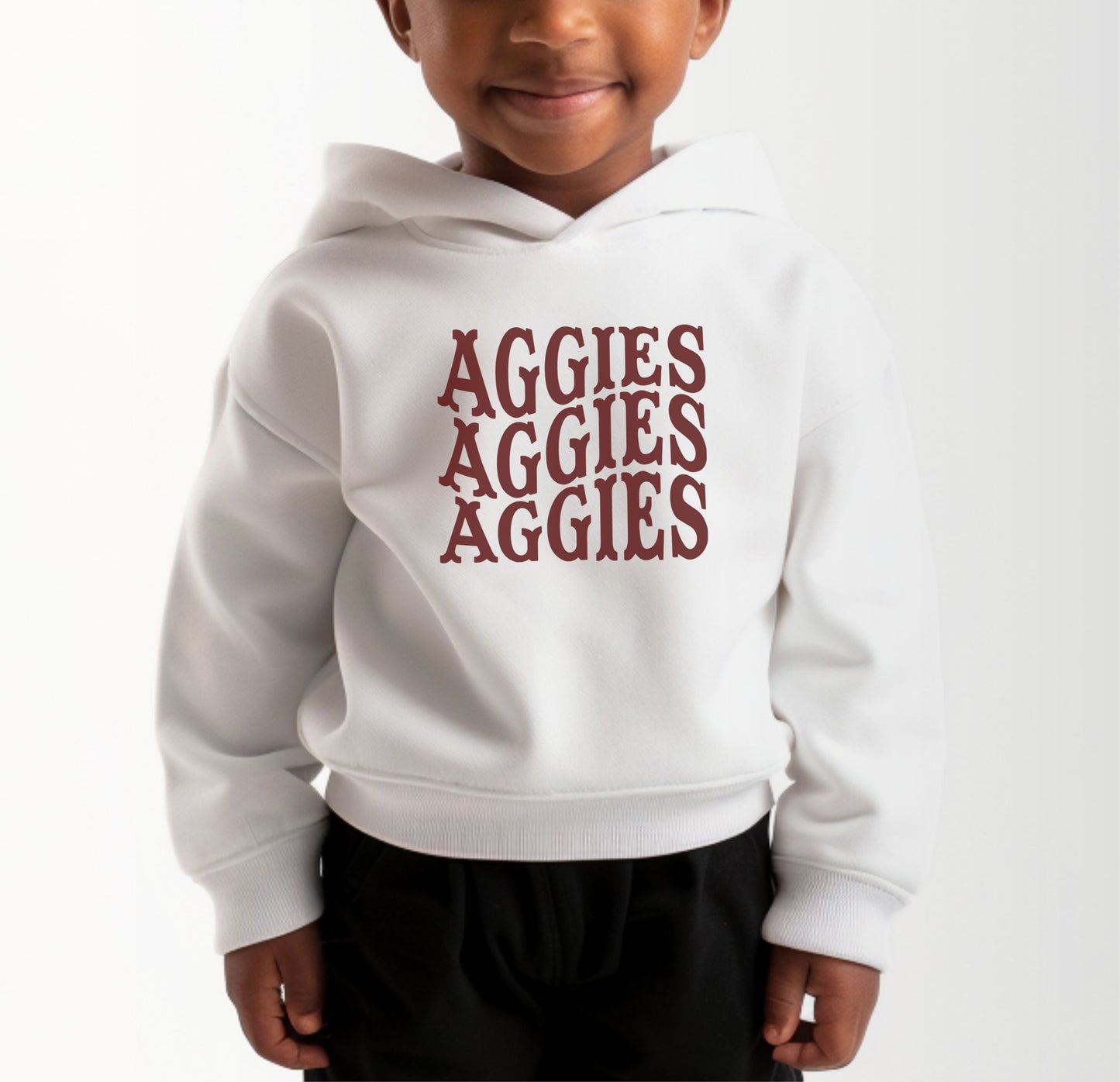 A model wears the White Toddler Unisex Texas A&M Aggies Aggies Aggies Western Hooded Sweatshirt.  The ﻿Texas A&M Aggies Aggies Aggies Western﻿ graphic is in bold Maroon in a Western style.