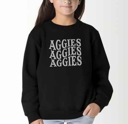 A model wears the Black Youth Unisex Texas A&M Aggies Aggies Aggies Western Crewneck Sweatshirt.  The ﻿Texas A&M Aggies Aggies Aggies Western﻿ graphic is in bold White in a Western style.