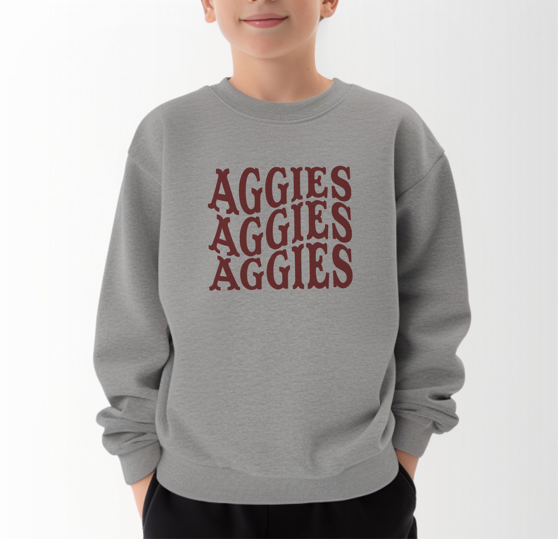 A model wears the Sport Grey Youth Unisex Texas A&M Aggies Aggies Aggies Western Crewneck Sweatshirt.  The ﻿Texas A&M Aggies Aggies Aggies Western﻿ graphic is in bold Maroon in a Western style.