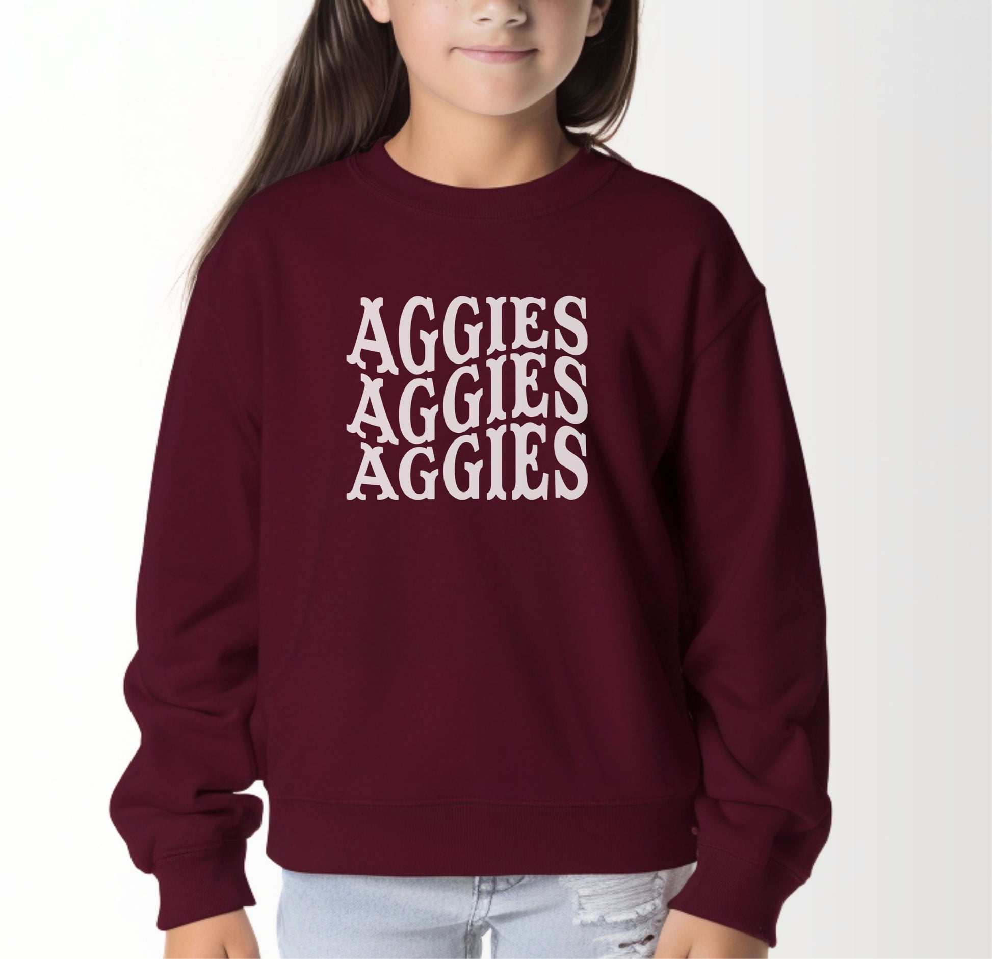 A model wears the Maroon Youth Unisex Texas A&M Aggies Aggies Aggies Western Crewneck Sweatshirt.  The ﻿Texas A&M Aggies Aggies Aggies Western﻿ graphic is in bold White in a Western style.