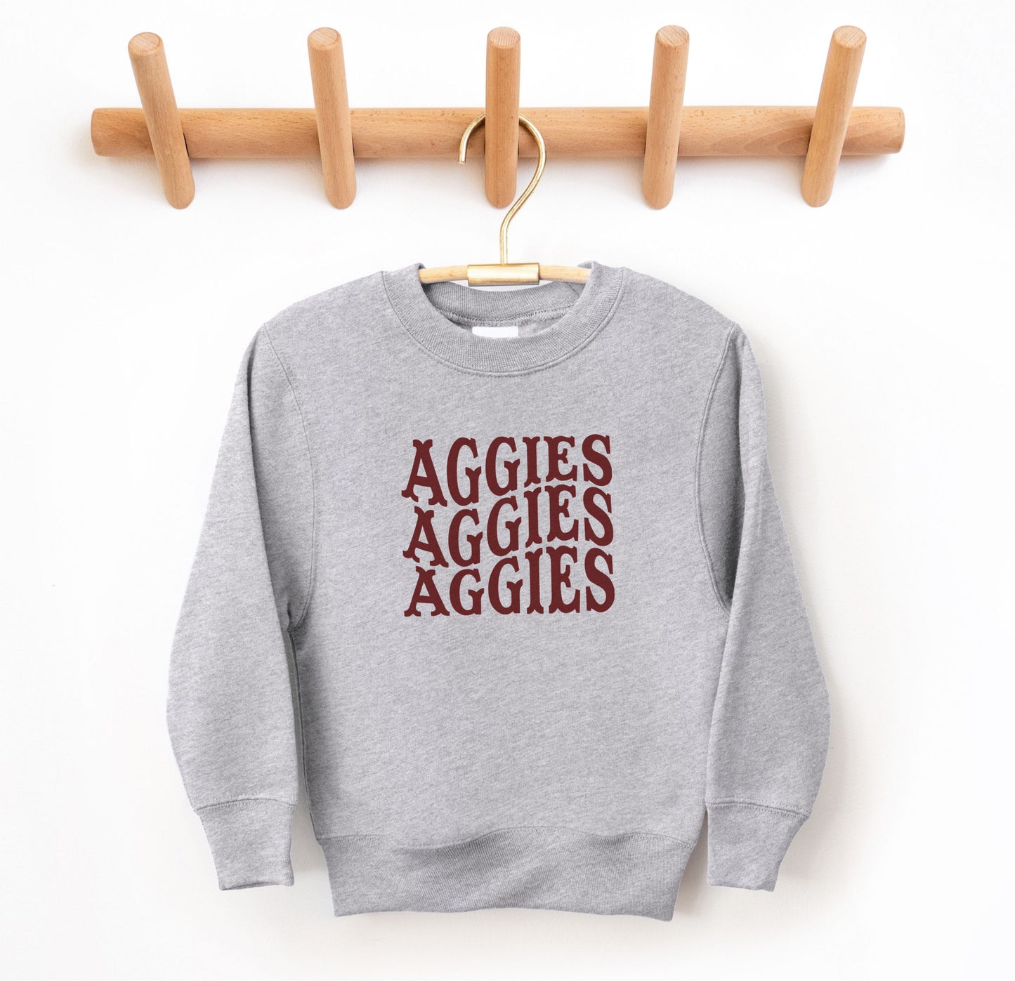 The Sport Grey Youth Unisex Texas A&M Aggies Aggies Aggies Western Crewneck Sweatshirt lays flat on a white background. The ﻿Texas A&M Aggies Aggies Aggies Western﻿ graphic is in bold Maroon in a Western style.