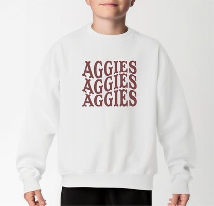 A model wears the White Youth Unisex Texas A&M Aggies Aggies Aggies Western Crewneck Sweatshirt.  The ﻿Texas A&M Aggies Aggies Aggies Western﻿ graphic is in bold Maroon in a Western style.