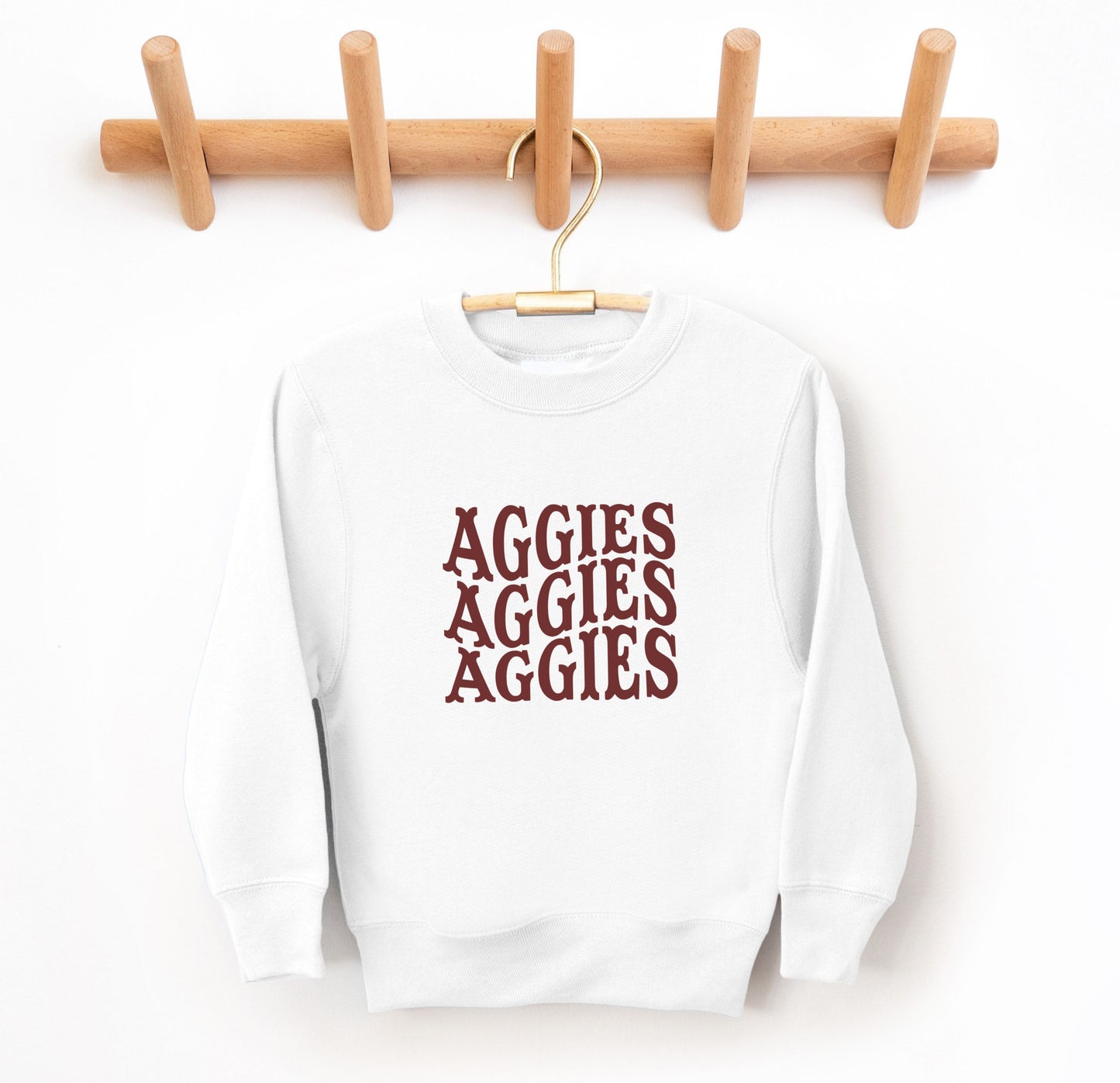 The White Youth Unisex Texas A&M Aggies Aggies Aggies Western Crewneck Sweatshirt lays flat on a white background. The ﻿Texas A&M Aggies Aggies Aggies Western﻿ graphic is in bold Maroon in a Western style.