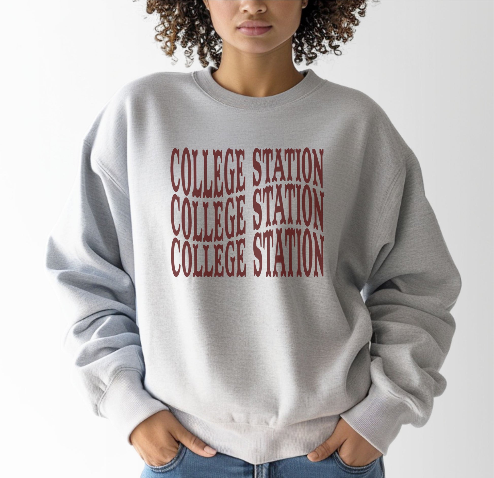 A model wears the Sport Grey Adult Unisex College Station Western Crewneck Sweatshirt.  The ﻿College Station Western﻿ graphic is in bold Maroon in a Western style.