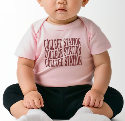 A model wears the Pink Infant Unisex College Station Western Bodysuit.  The ﻿College Station Western﻿ graphic is in bold Maroon in a Western style.