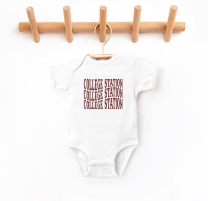 The White Infant Unisex College Station Western Bodysuit lays flat on a white background. The ﻿College Station Western﻿ graphic is in bold Maroon in a Western style.