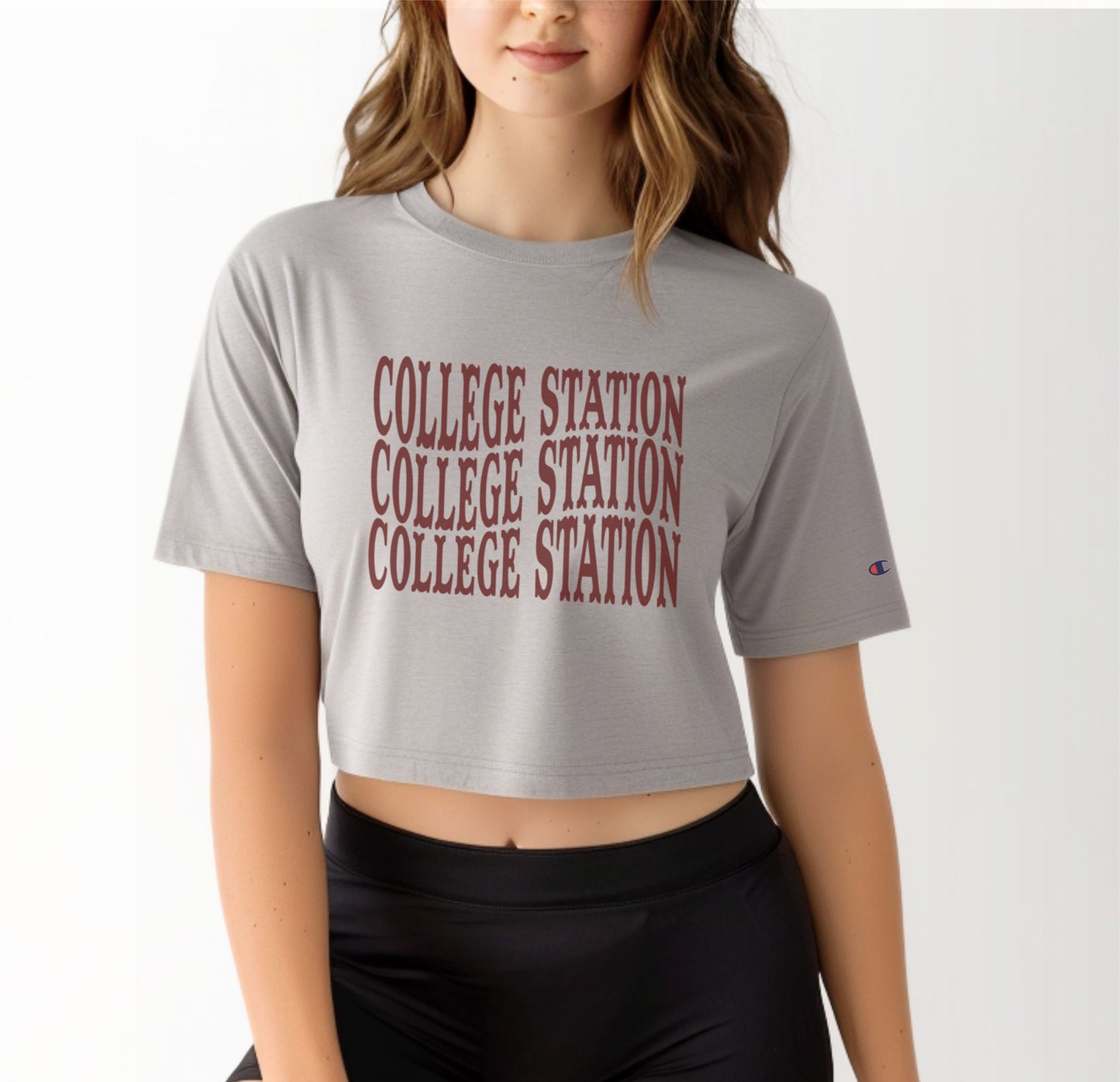 A model wears the Oxford Grey Adult Womens College Station Western Crop Top.  The ﻿College Station Western﻿ graphic is in bold Maroon in a Western style.