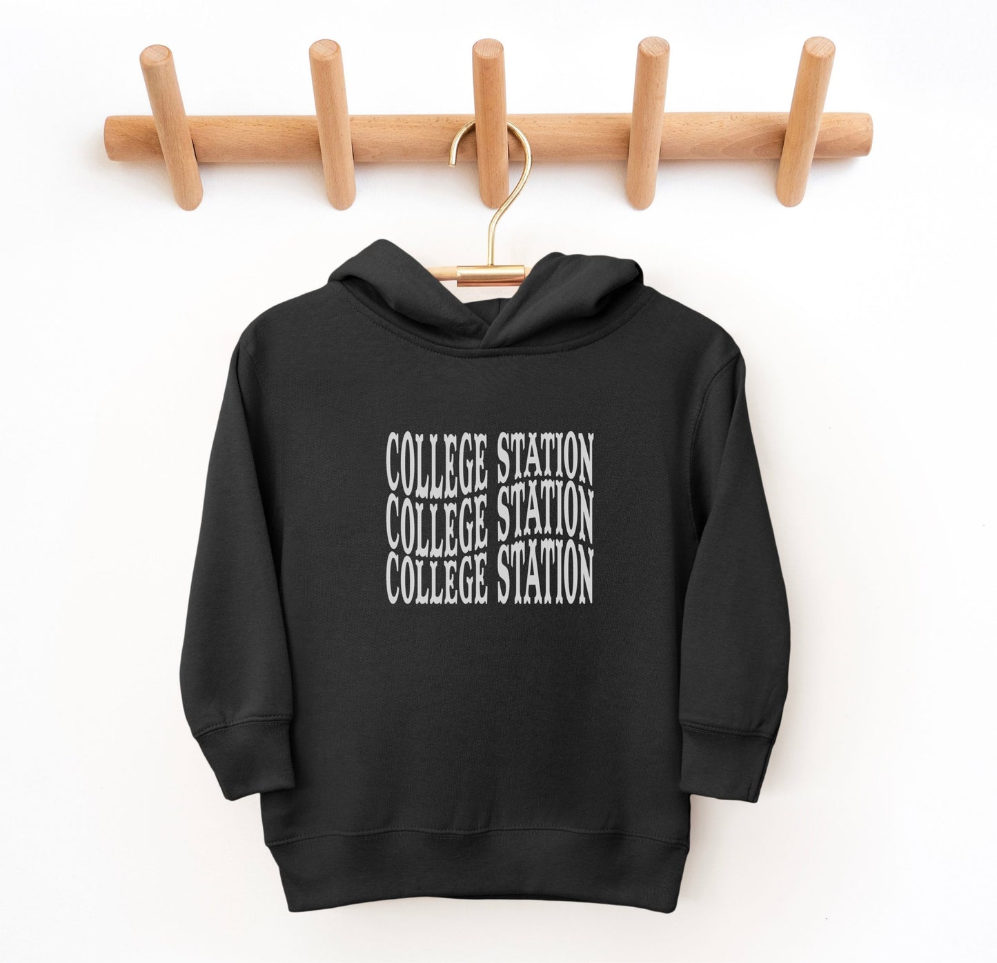 The Black Toddler Unisex College Station Western Hooded Sweatshirt lays flat on a white background. The ﻿College Station Western﻿ graphic is in bold White in a Western style.