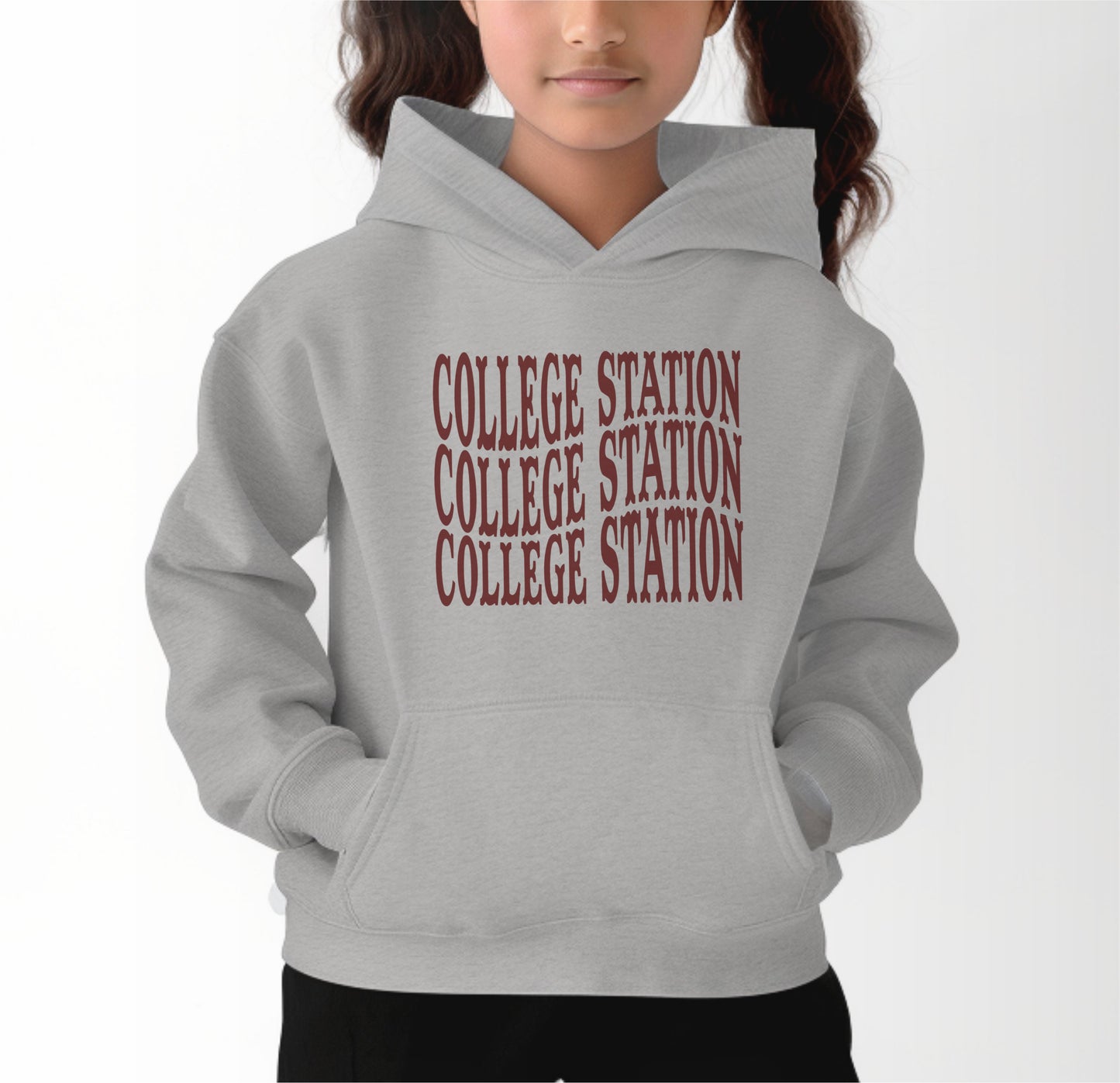 A model wears the Sport Grey Youth Unisex College Station Western Hooded Sweatshirt.  The ﻿College Station Western﻿ graphic is in bold Maroon in a Western style.