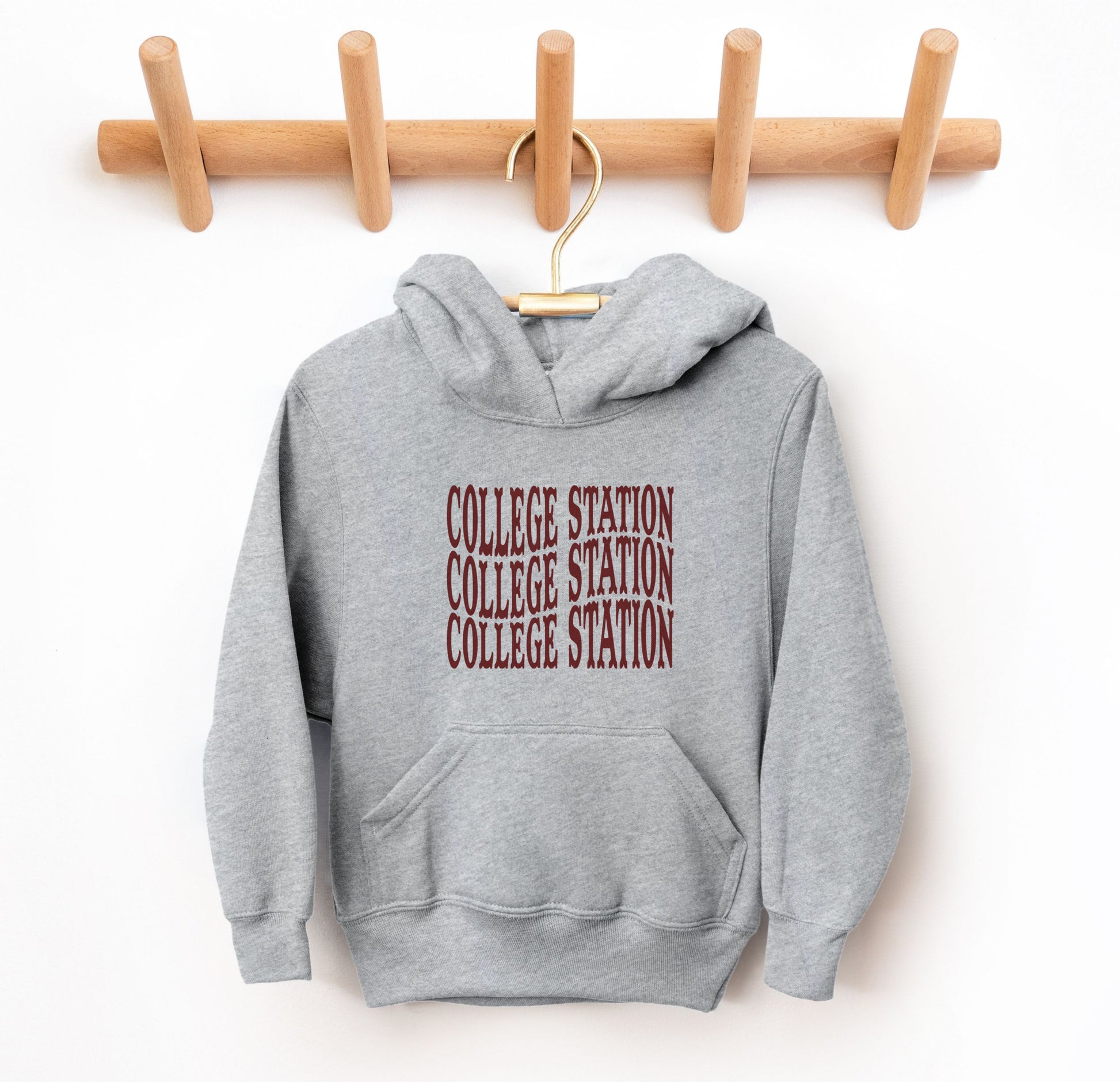 The Heather Youth Unisex College Station Western Hooded Sweatshirt lays flat on a white background. The ﻿College Station Western﻿ graphic is in bold Maroon in a Western style.