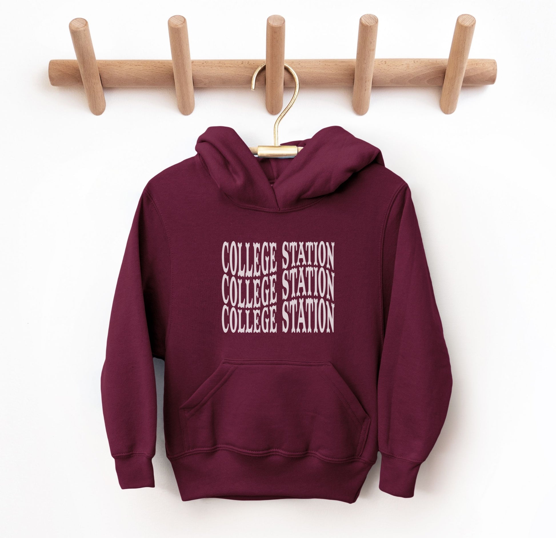 The Maroon Youth Unisex College Station Western Hooded Sweatshirt lays flat on a white background. The ﻿College Station Western﻿ graphic is in bold White in a Western style.