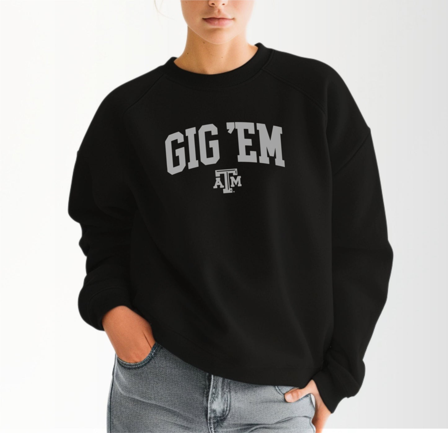 A model wears the Black Adult Unisex Texas A&M Gig 'Em Collegiate Crewneck Sweatshirt.  The ﻿Texas A&M Gig 'Em Collegiate﻿ graphic is in bold White in a Collegiate style.