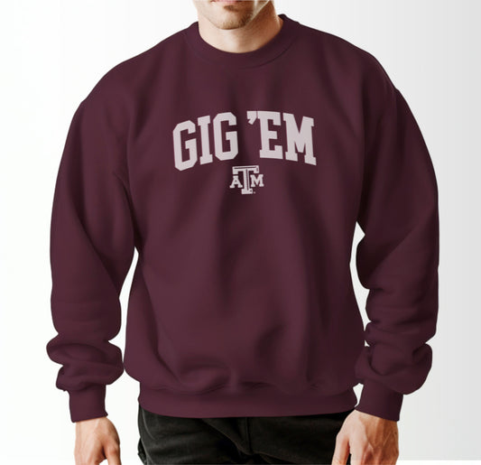 A model wears the Maroon Adult Unisex Texas A&M Gig 'Em Collegiate Crewneck Sweatshirt.  The ﻿Texas A&M Gig 'Em Collegiate﻿ graphic is in bold White in a Collegiate style.