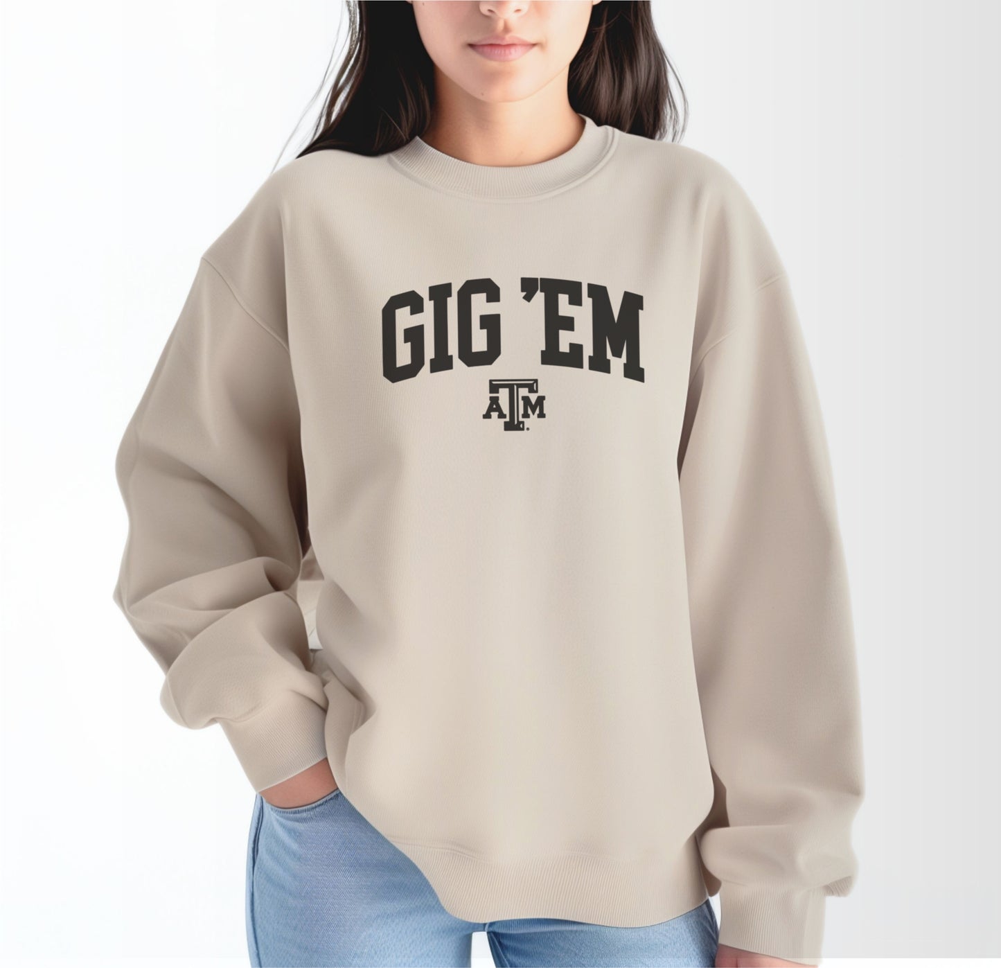 A model wears the Sand Adult Unisex Texas A&M Gig 'Em Collegiate Crewneck Sweatshirt.  The ﻿Texas A&M Gig 'Em Collegiate﻿ graphic is in bold Black in a Collegiate style.