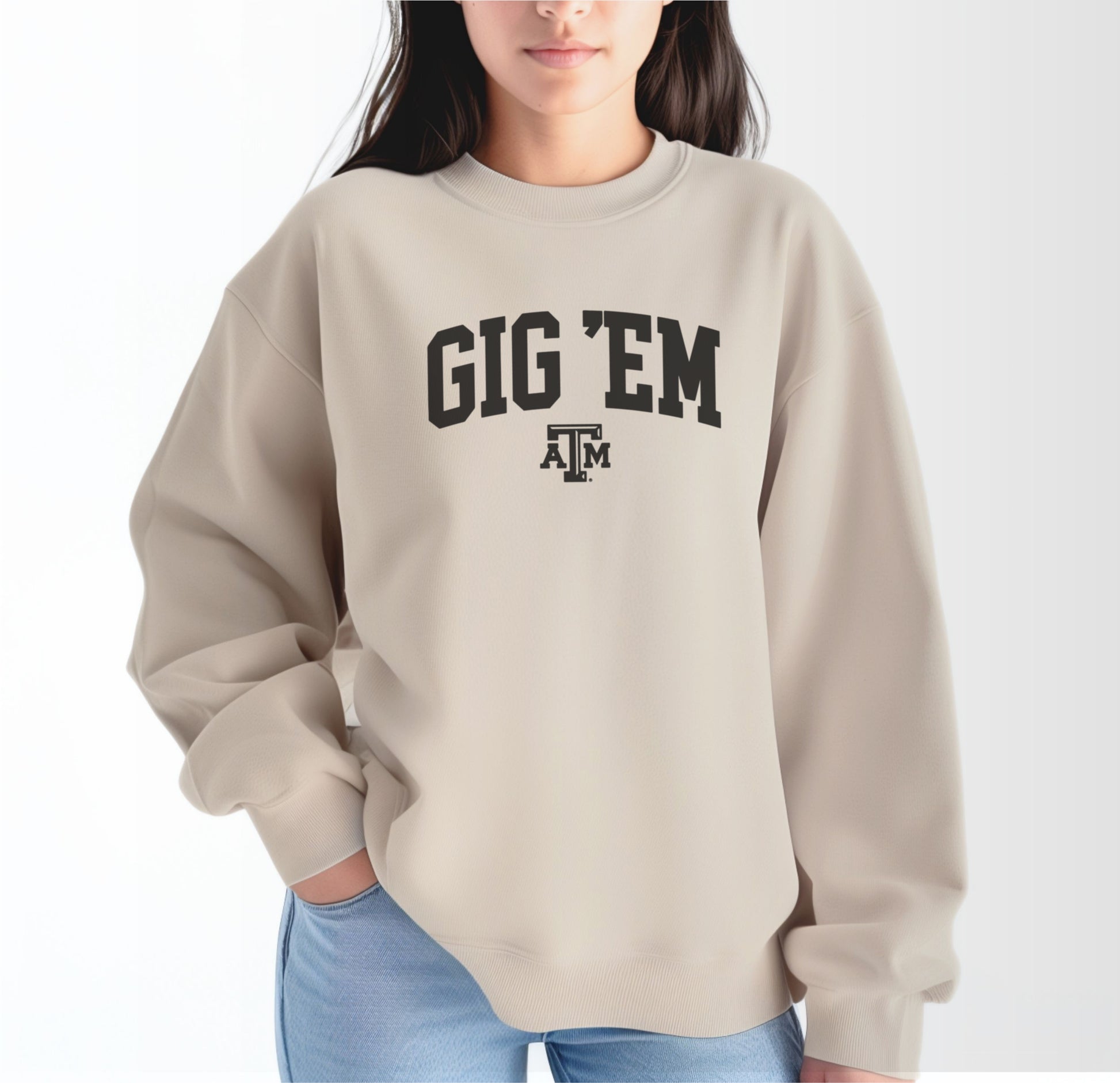 A model wears the Sand Adult Unisex Texas A&M Gig 'Em Collegiate Crewneck Sweatshirt.  The ﻿Texas A&M Gig 'Em Collegiate﻿ graphic is in bold Black in a Collegiate style.