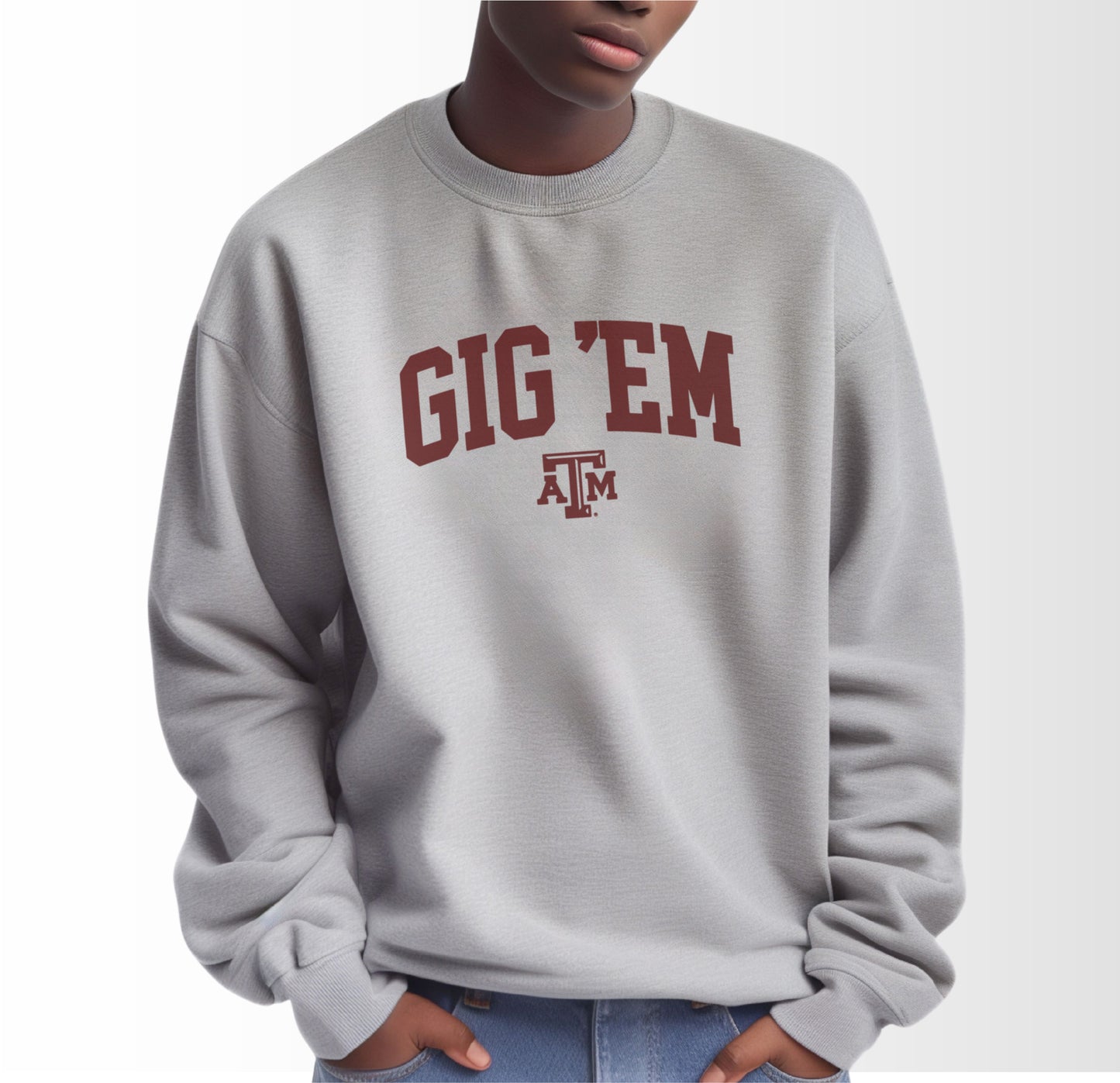 A model wears the Sport Grey Adult Unisex Texas A&M Gig 'Em Collegiate Crewneck Sweatshirt.  The ﻿Texas A&M Gig 'Em Collegiate﻿ graphic is in bold Maroon in a Collegiate style.