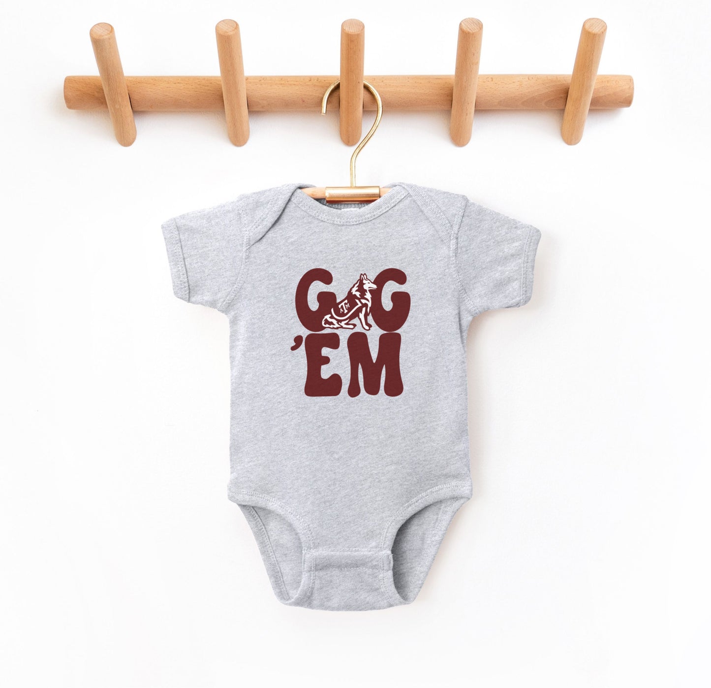 The Heather Grey Infant Unisex Texas A&M Gig 'Em Retro Reveille Bodysuit lays flat on a white background. The ﻿Texas A&M Gig 'Em Retro Reveille﻿ graphic is in bold Maroon in a Groovy Vintage style.