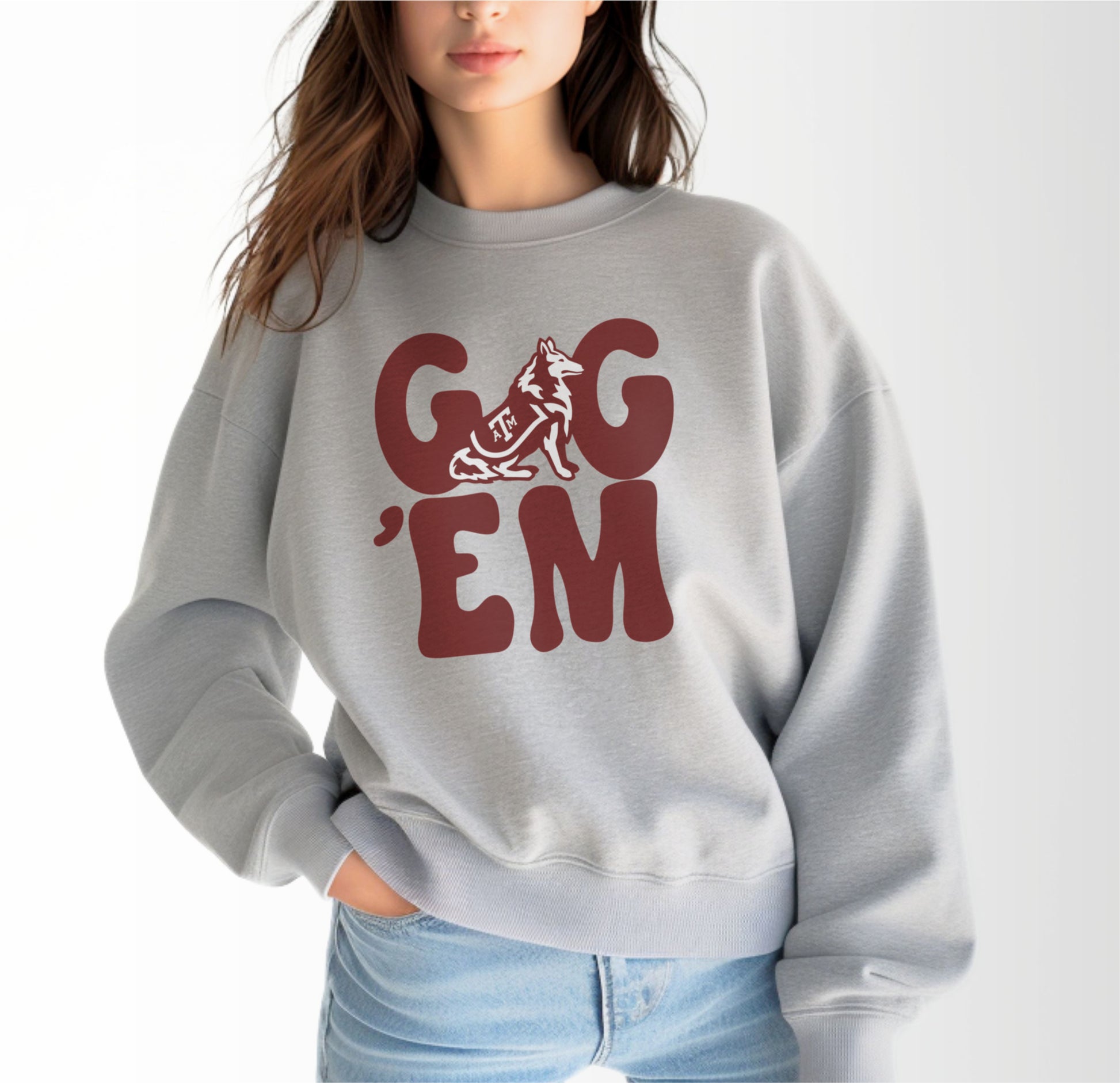 A model wears the Sport Grey Adult Unisex Texas A&M Gig 'Em Retro Reveille Crewneck Sweatshirt.  The ﻿Texas A&M Gig 'Em Retro Reveille﻿ graphic is in bold Maroon in a Groovy Vintage style.