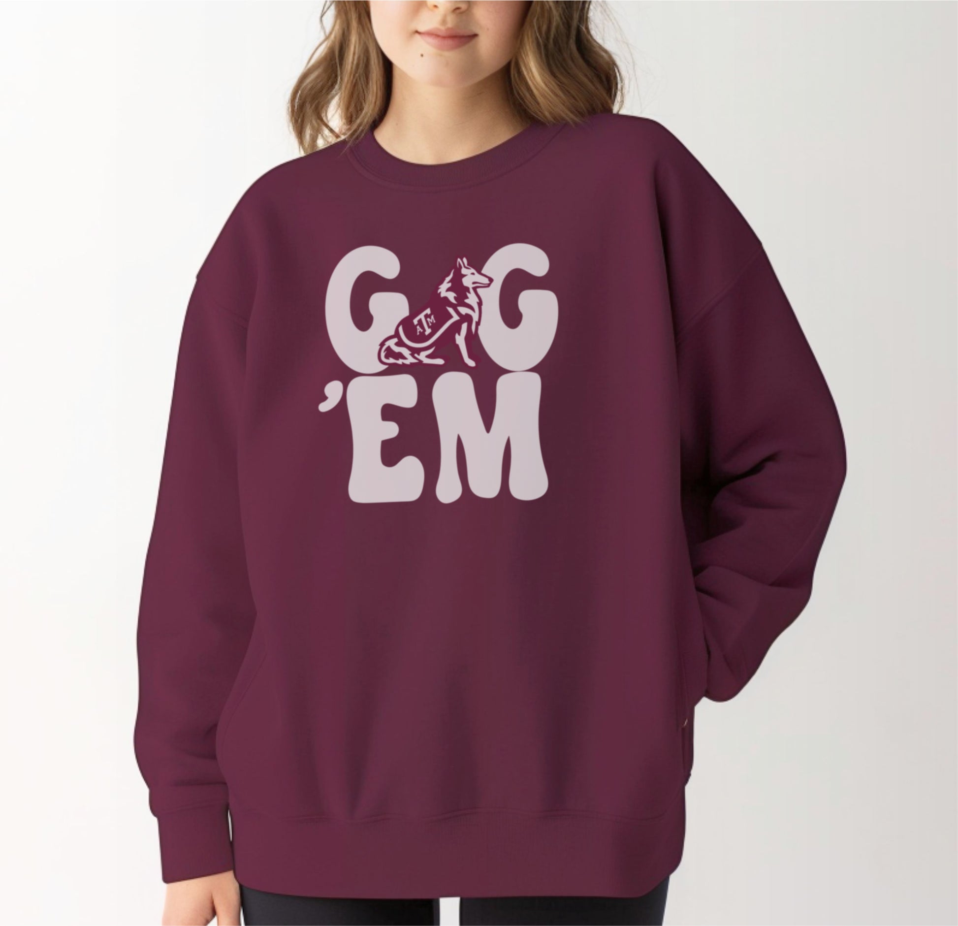 A model wears the Maroon Adult Unisex Texas A&M Gig 'Em Retro Reveille Crewneck Sweatshirt.  The ﻿Texas A&M Gig 'Em Retro Reveille﻿ graphic is in bold White in a Groovy Vintage style.