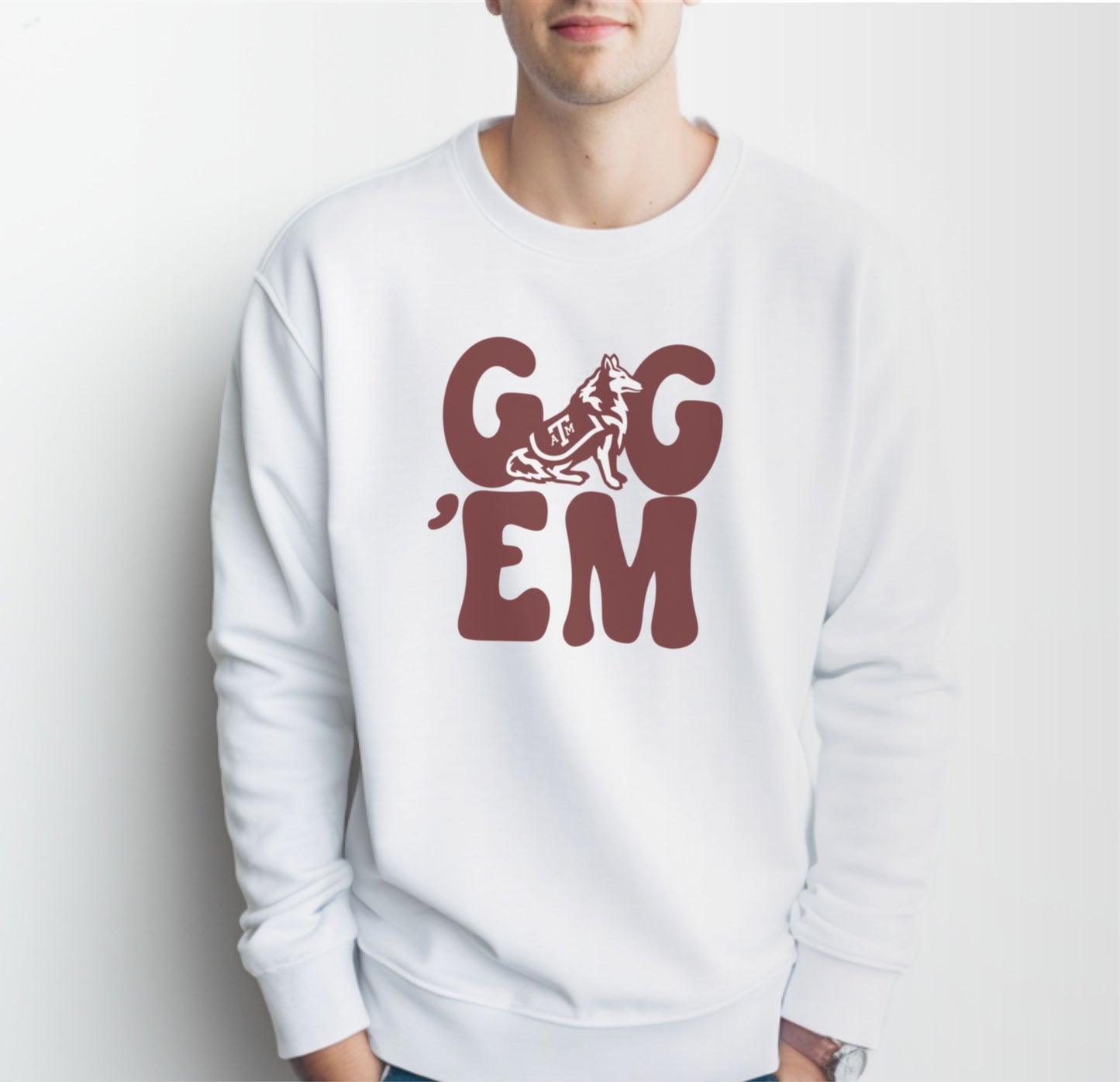 A model wears the White Adult Unisex Texas A&M Gig 'Em Retro Reveille Crewneck Sweatshirt.  The ﻿Texas A&M Gig 'Em Retro Reveille﻿ graphic is in bold Maroon in a Groovy Vintage style.