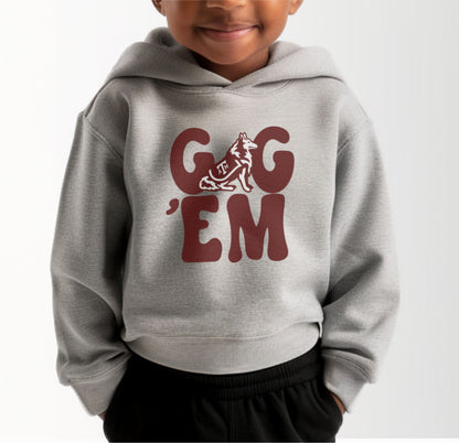 A model wears the Heather Grey Toddler Unisex Texas A&M Gig 'Em Retro Reveille Hooded Sweatshirt.  The ﻿Texas A&M Gig 'Em Retro Reveille﻿ graphic is in bold Maroon in a Groovy Vintage style.