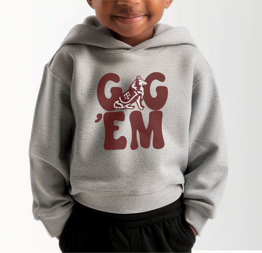A model wears the Heather Grey Toddler Unisex Texas A&M Gig 'Em Retro Reveille Hooded Sweatshirt.  The ﻿Texas A&M Gig 'Em Retro Reveille﻿ graphic is in bold Maroon in a Groovy Vintage style.