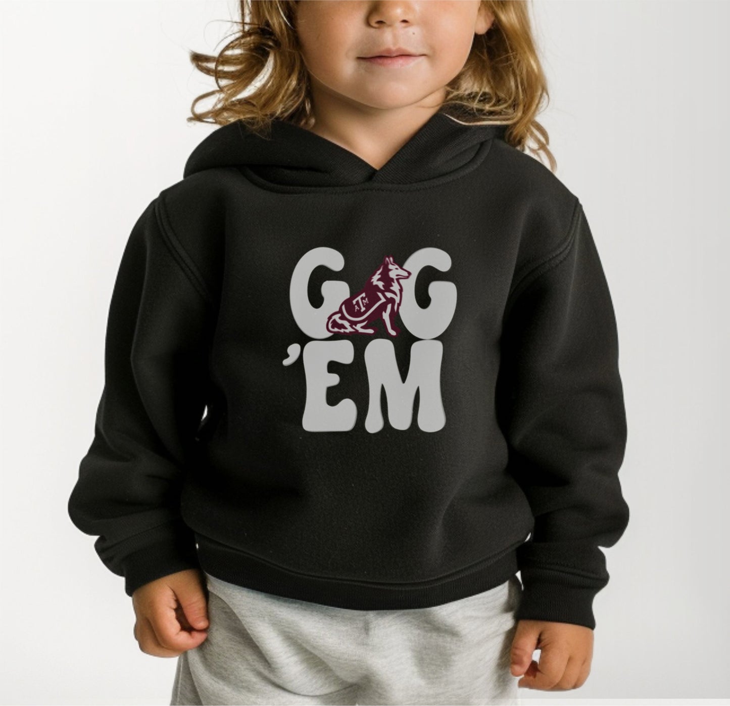 A model wears the Black Toddler Unisex Texas A&M Gig 'Em Retro Reveille Hooded Sweatshirt.  The ﻿Texas A&M Gig 'Em Retro Reveille﻿ graphic is in bold White in a Groovy Vintage style.