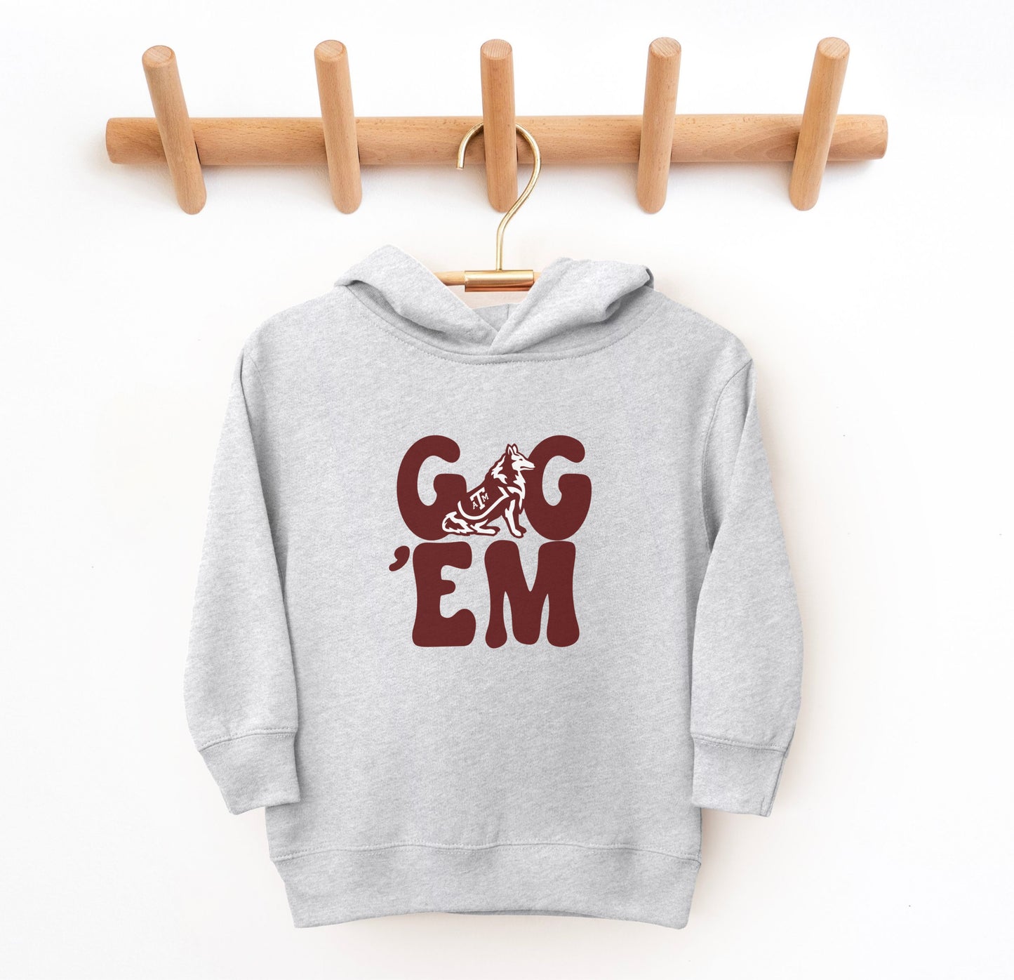 The Heather Grey Toddler Unisex Texas A&M Gig 'Em Retro Reveille Hooded Sweatshirt lays flat on a white background. The ﻿Texas A&M Gig 'Em Retro Reveille﻿ graphic is in bold Maroon in a Groovy Vintage style.