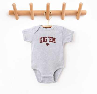 The Heather Grey Infant Unisex Texas A&M Gig 'Em Collegiate Bodysuit lays flat on a white background. The ﻿Texas A&M Gig 'Em Collegiate﻿ graphic is in bold Maroon in a Collegiate style.