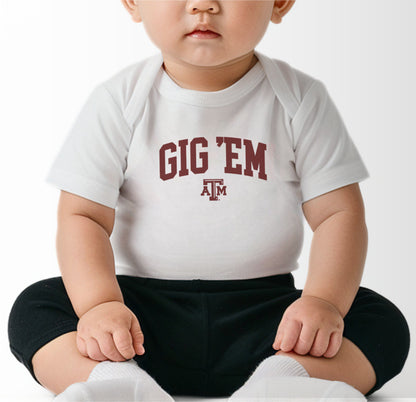 A model wears the Black Infant Unisex Texas A&M Gig 'Em Collegiate Bodysuit.  The ﻿Texas A&M Gig 'Em Collegiate﻿ graphic is in bold White in a Collegiate style.