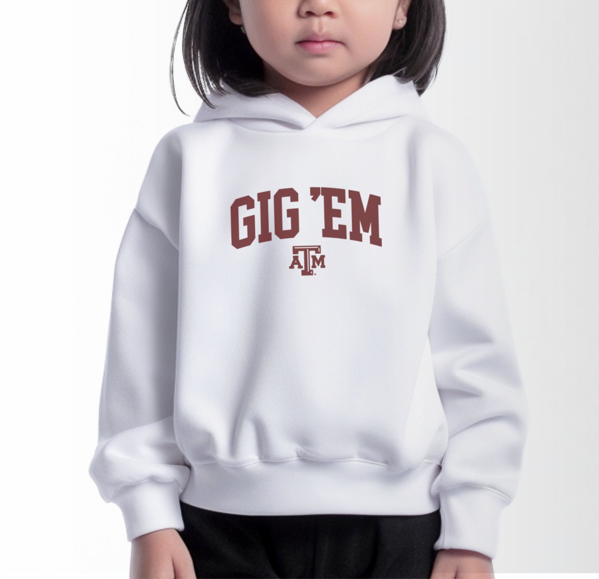 A model wears the White Toddler Unisex Texas A&M Gig 'Em Collegiate Hooded Sweatshirt.  The ﻿Texas A&M Gig 'Em Collegiate﻿ graphic is in bold Maroon in a Collegiate style.