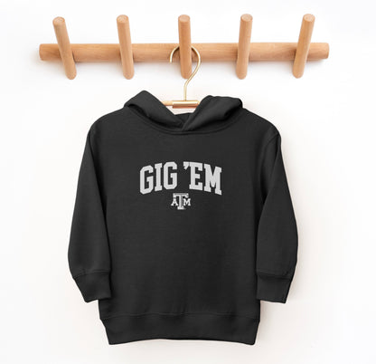 The Black Toddler Unisex Texas A&M Gig 'Em Collegiate Hooded Sweatshirt lays flat on a white background. The ﻿Texas A&M Gig 'Em Collegiate﻿ graphic is in bold White in a Collegiate style.