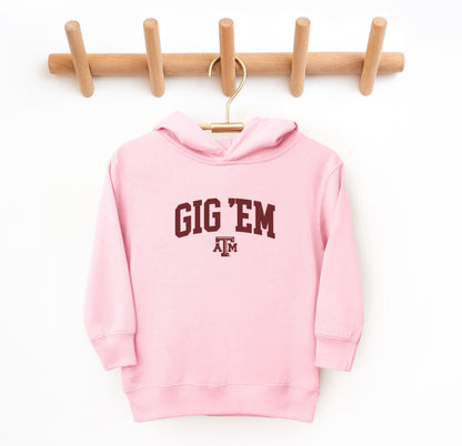 The Pink Toddler Unisex Texas A&M Gig 'Em Collegiate Hooded Sweatshirt lays flat on a white background. The ﻿Texas A&M Gig 'Em Collegiate﻿ graphic is in bold White in a Collegiate style.