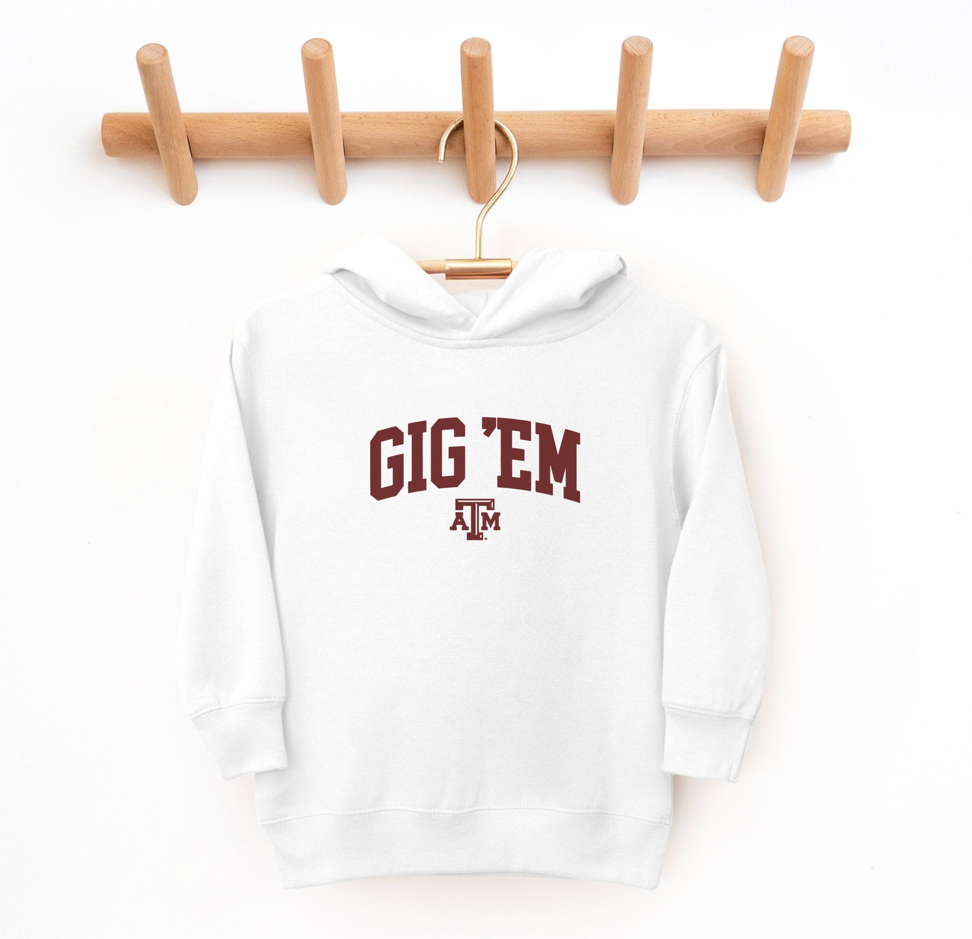 The White Toddler Unisex Texas A&M Gig 'Em Collegiate Hooded Sweatshirt lays flat on a white background. The ﻿Texas A&M Gig 'Em Collegiate﻿ graphic is in bold Maroon in a Collegiate style.