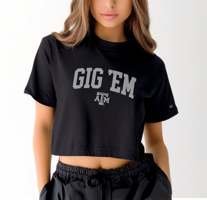 A model wears the Black Adult Womens Texas A&M Gig 'Em Collegiate Crop Top.  The ﻿Texas A&M Gig 'Em Collegiate﻿ graphic is in bold White in a Collegiate style.