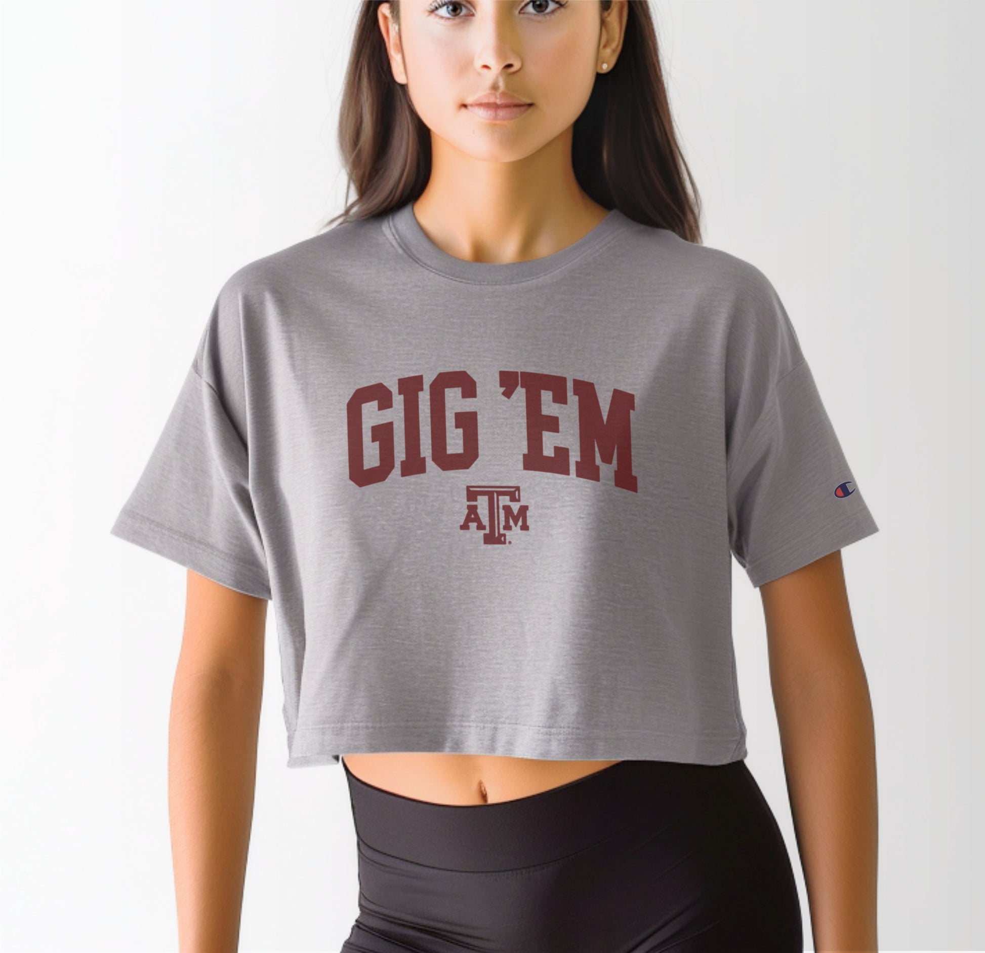 A model wears the Oxford Grey Adult Womens Texas A&M Gig 'Em Collegiate Crop Top.  The ﻿Texas A&M Gig 'Em Collegiate﻿ graphic is in bold Maroon in a Collegiate style.