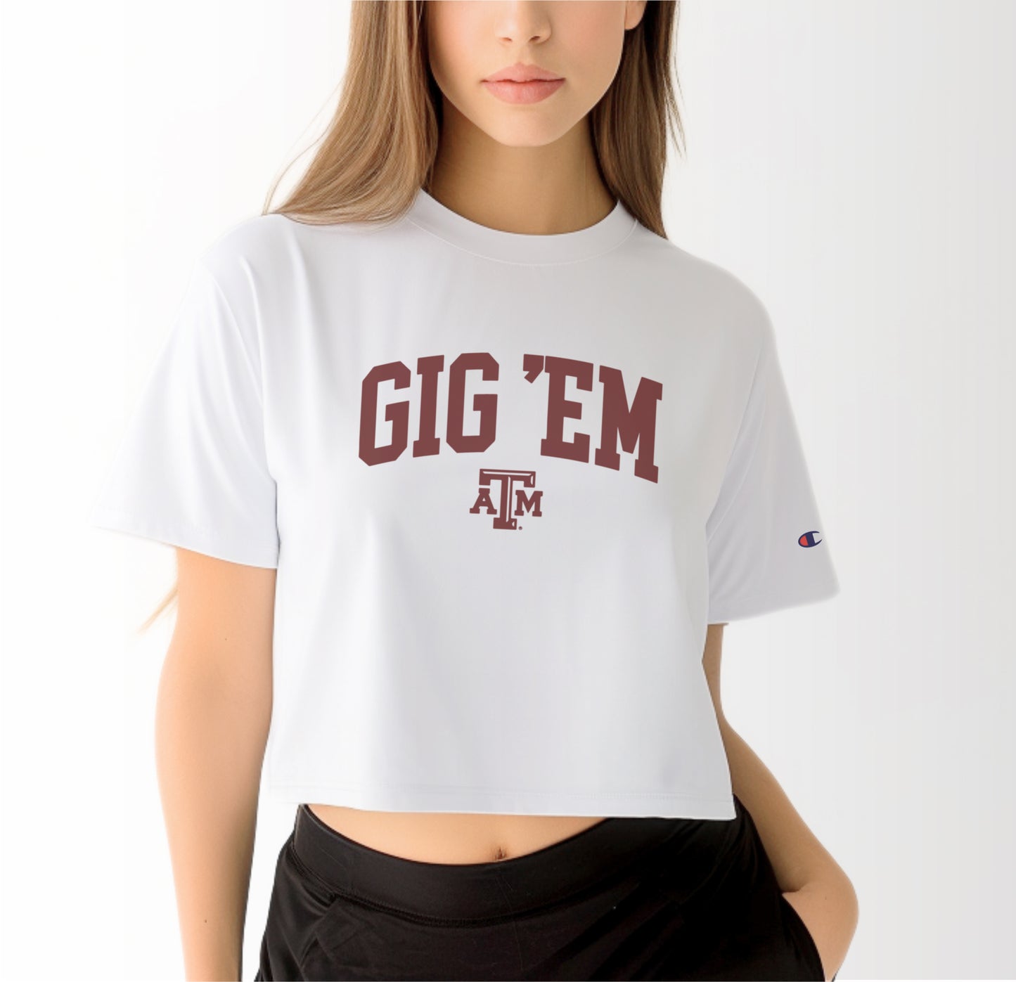 A model wears the White Adult Womens Texas A&M Gig 'Em Collegiate Crop Top.  The ﻿Texas A&M Gig 'Em Collegiate﻿ graphic is in bold Maroon in a Collegiate style.