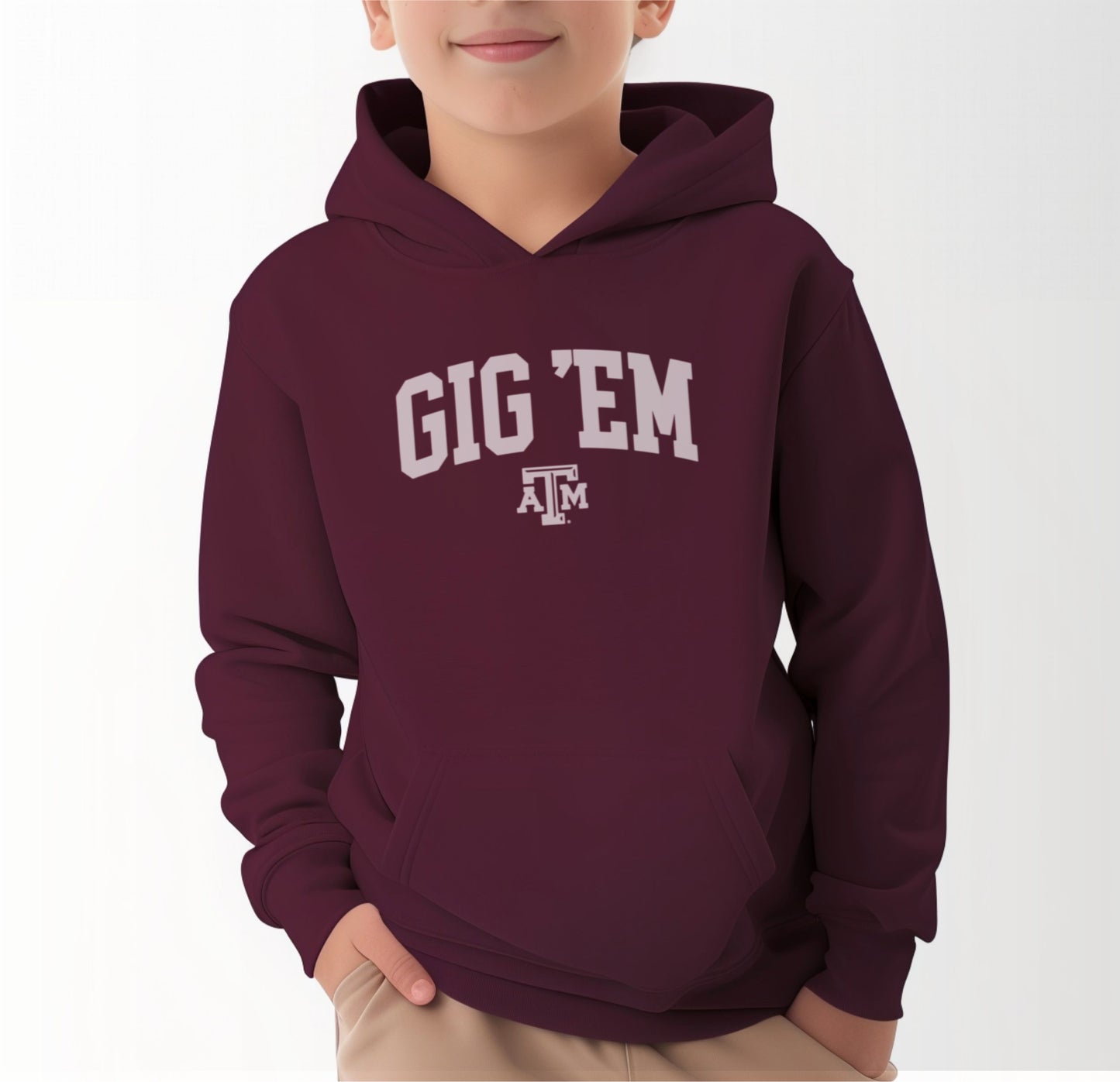 A model wears the Maroon Youth Unisex Texas A&M Gig 'Em Collegiate Hooded Sweatshirt.  The ﻿Texas A&M Gig 'Em Collegiate﻿ graphic is in bold White in a Collegiate style.