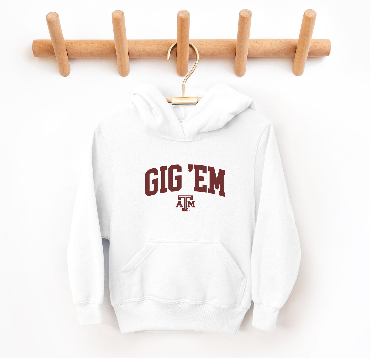 The White Youth Unisex Texas A&M Gig 'Em Collegiate Hooded Sweatshirt lays flat on a white background. The ﻿Texas A&M Gig 'Em Collegiate﻿ graphic is in bold Maroon in a Collegiate style.