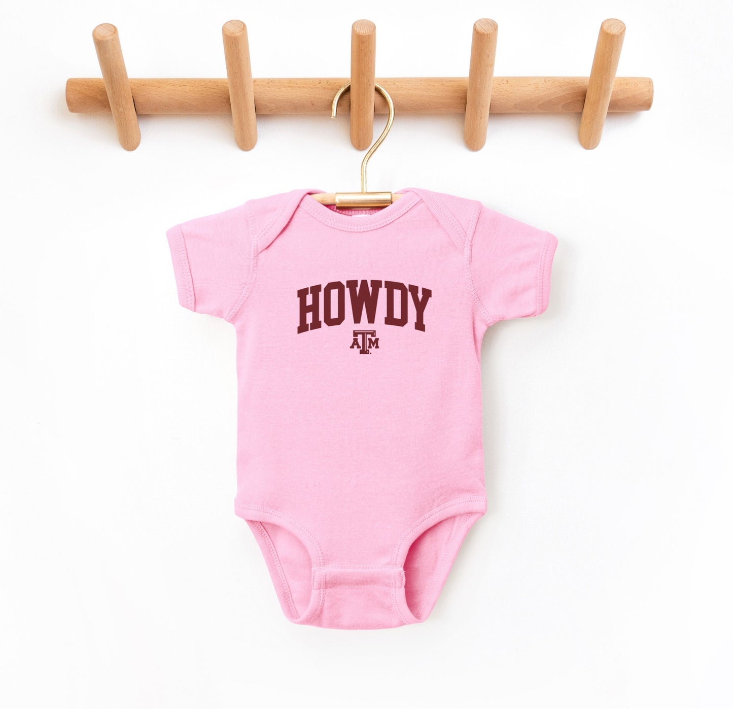 The Pink Infant Unisex Texas A&M Howdy Varsity Bodysuit lays flat on a white background. The ﻿Texas A&M Howdy Varsity﻿ graphic is in bold Maroon in a Collegiate style.