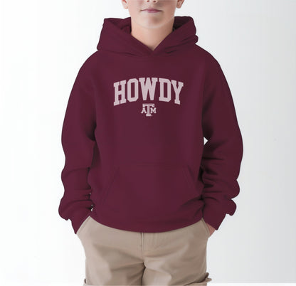 A model wears the Maroon Youth Unisex Texas A&M Howdy Varsity Hooded Sweatshirt.  The ﻿Texas A&M Howdy Varsity﻿ graphic is in bold White in a Collegiate style.