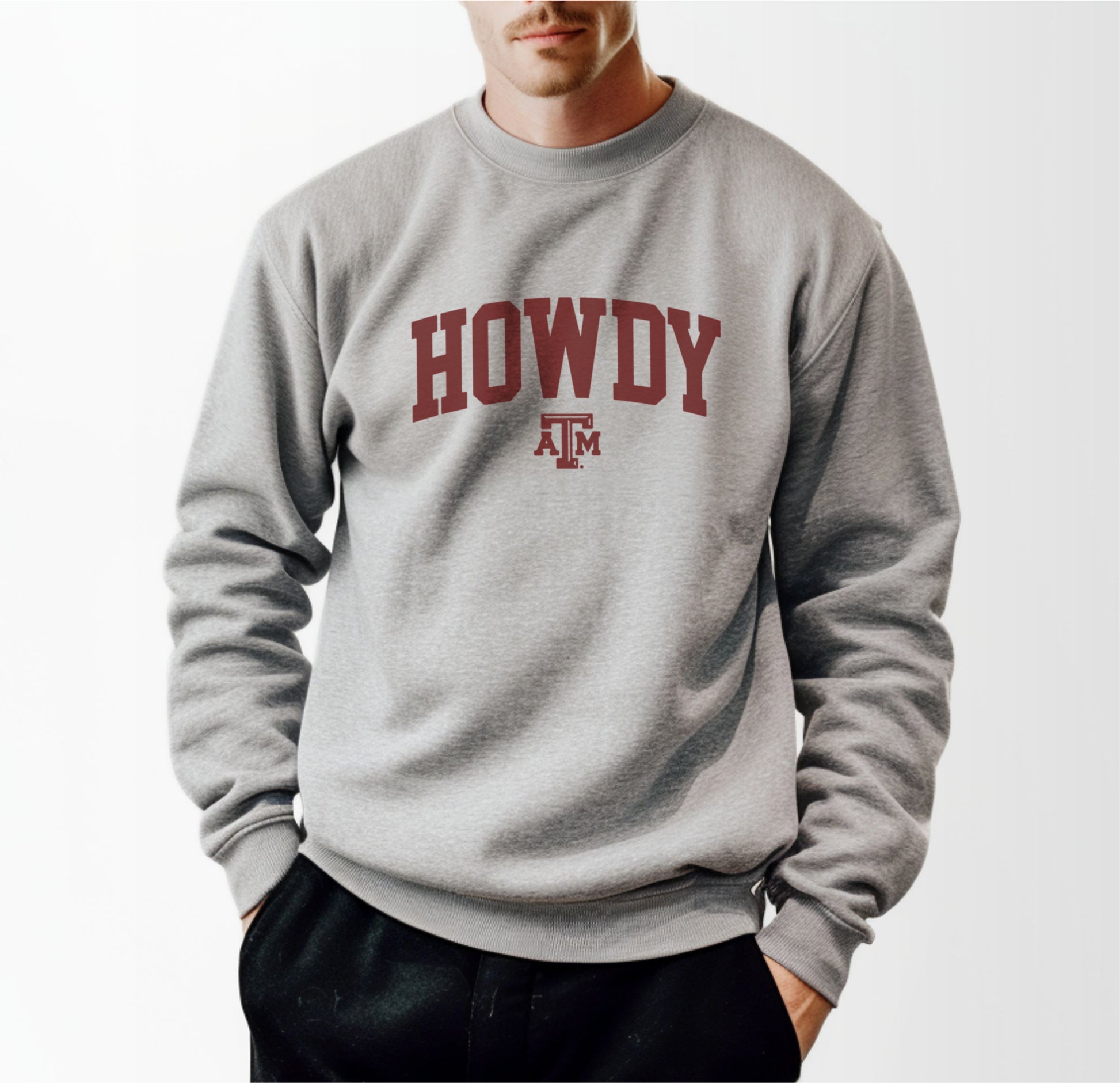 A model wears the Sport Grey Adult Unisex Texas A&M Howdy Varsity Crewneck Sweatshirt.  The ﻿Texas A&M Howdy Varsity﻿ graphic is in bold Maroon in a Collegiate style.