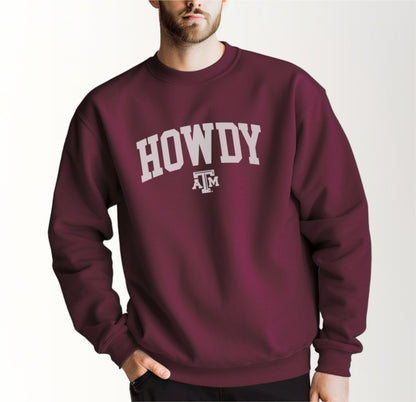 A model wears the Maroon Adult Unisex Texas A&M Howdy Varsity Crewneck Sweatshirt.  The ﻿Texas A&M Howdy Varsity﻿ graphic is in bold White in a Collegiate style.