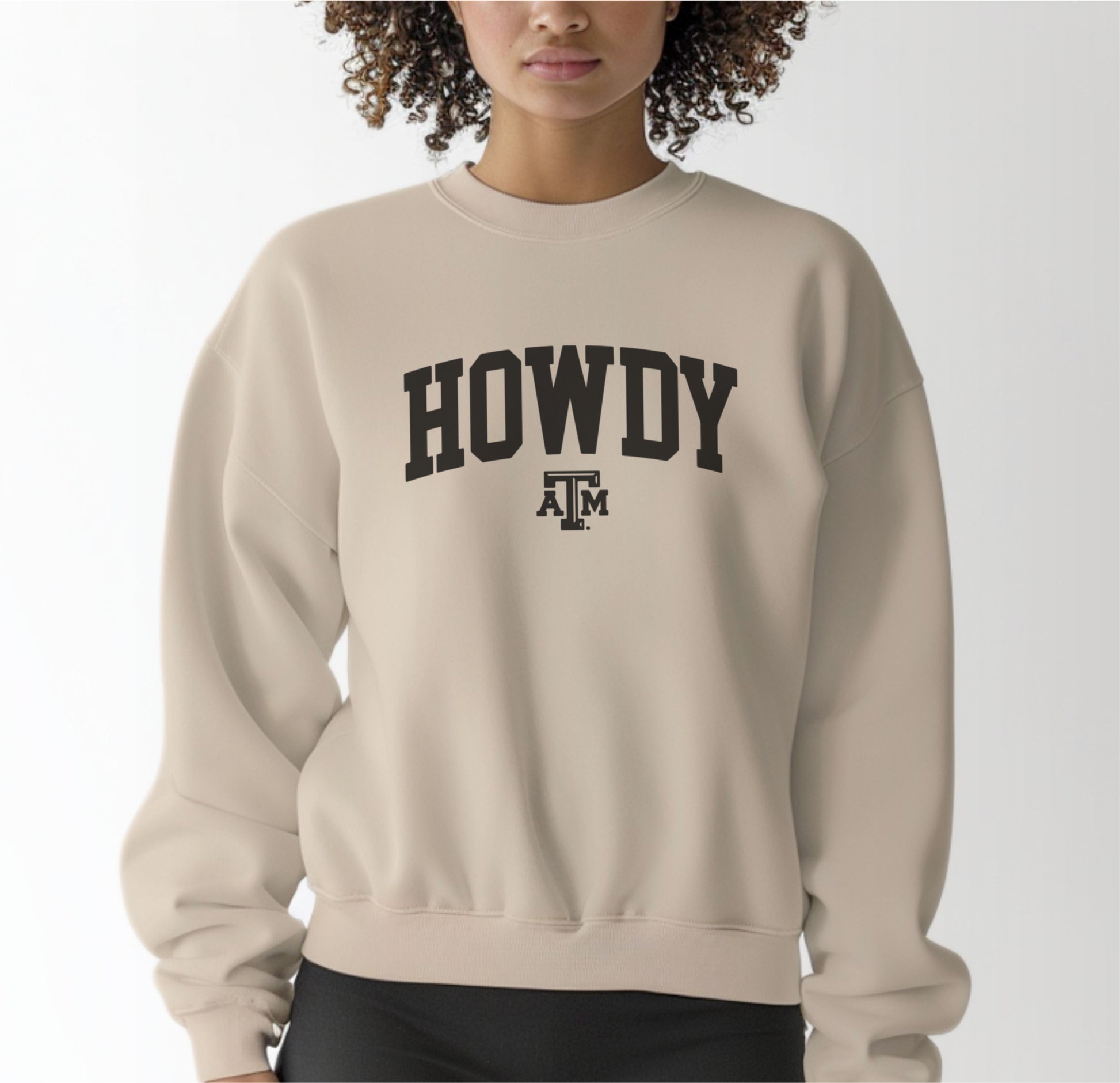 A model wears the Sand Adult Unisex Texas A&M Howdy Varsity Crewneck Sweatshirt.  The ﻿Texas A&M Howdy Varsity﻿ graphic is in bold Black in a Collegiate style.