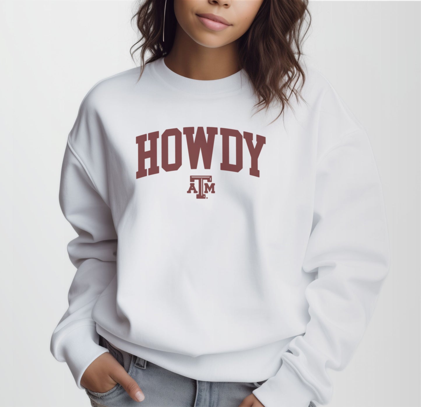 A model wears the White Adult Unisex Texas A&M Howdy Varsity Crewneck Sweatshirt.  The ﻿Texas A&M Howdy Varsity﻿ graphic is in bold Maroon in a Collegiate style.