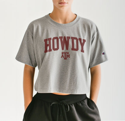 A model wears the Oxford Grey Adult Womens Texas A&M Howdy Varsity Crop Top.  The ﻿Texas A&M Howdy Varsity﻿ graphic is in bold Maroon in a Collegiate style.