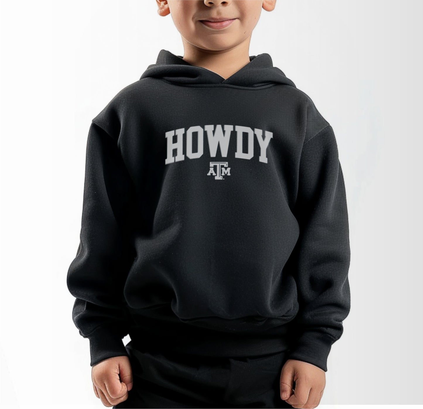 A model wears the Black Toddler Unisex Texas A&M Howdy Varsity Hooded Sweatshirt.  The ﻿Texas A&M Howdy Varsity﻿ graphic is in bold White in a Collegiate style.