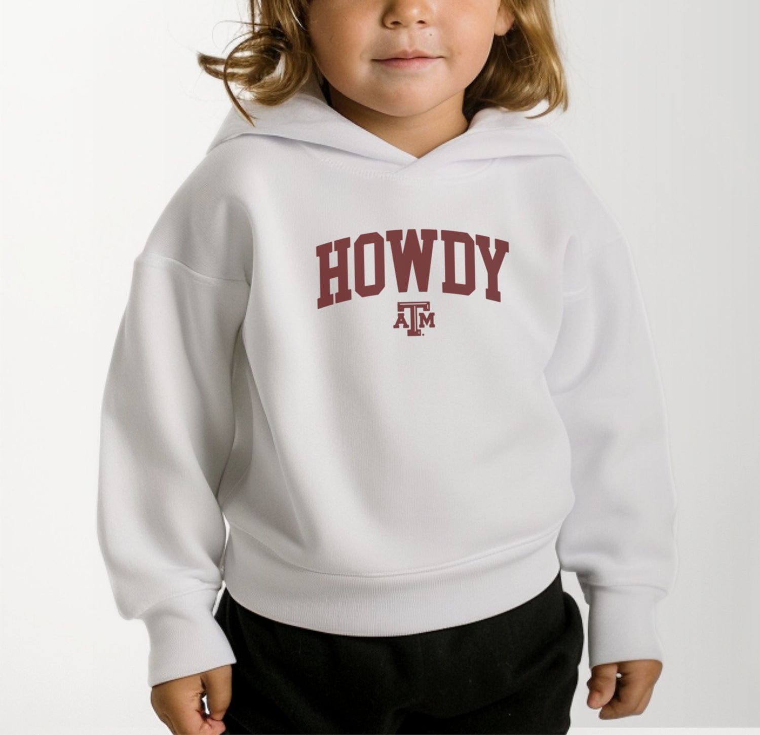 A model wears the White Toddler Unisex Texas A&M Howdy Varsity Hooded Sweatshirt.  The ﻿Texas A&M Howdy Varsity﻿ graphic is in bold Maroon in a Collegiate style.