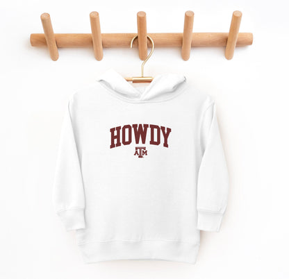 The White Toddler Unisex Texas A&M Howdy Varsity Hooded Sweatshirt lays flat on a white background. The ﻿Texas A&M Howdy Varsity﻿ graphic is in bold Maroon in a Collegiate style.