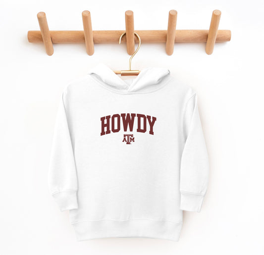 The White Toddler Unisex Texas A&M Howdy Varsity Hooded Sweatshirt lays flat on a white background. The ﻿Texas A&M Howdy Varsity﻿ graphic is in bold Maroon in a Collegiate style.